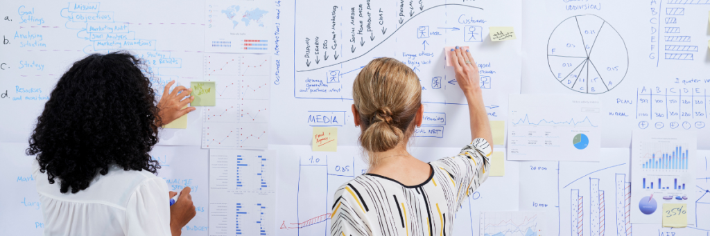 2 women working on graphs and charts at a whiteboard